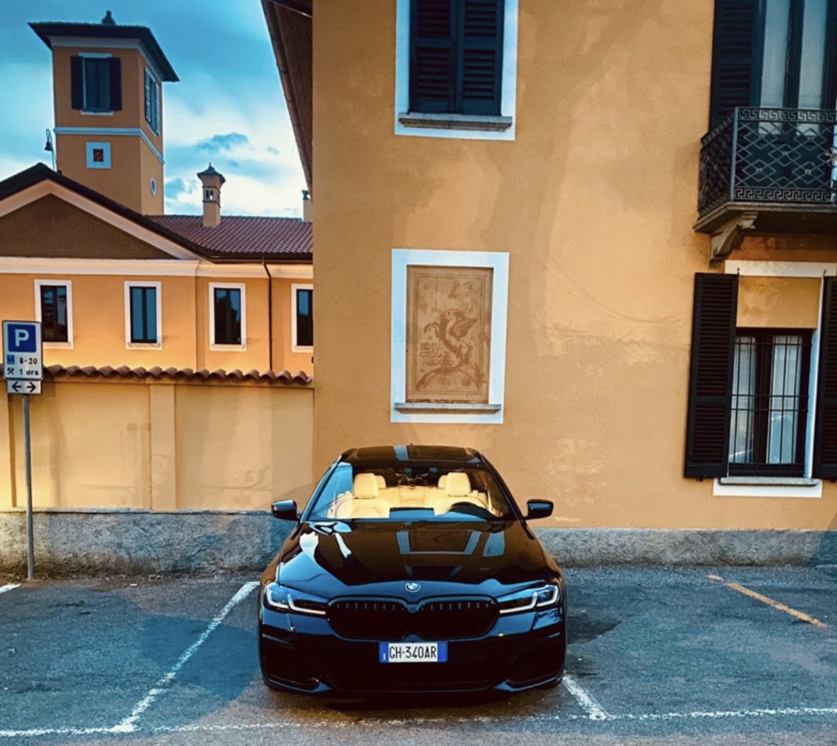 Berlina BMW nera con interni in pelle beige parcheggiata davanti a un edificio ocra con persiane scure e torretta